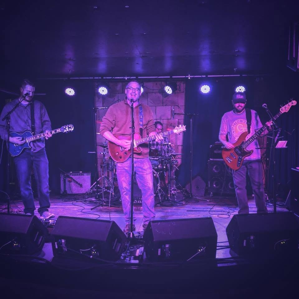 Knucklehorn on a club stage under coloured lights, with monitor wedges across the front